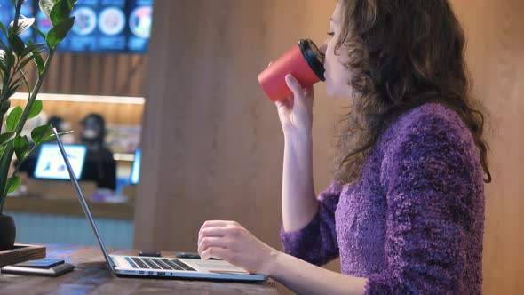 Slim Young Woman Drinks Coffee and Works on Laptop in Cafe