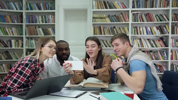 Smiling Attractive four Multiracial Friends which Watching on Girl's Phone in the Reading Room