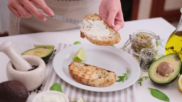 Woman Standing at Kitchen Spreading Whizzed Cream Cheese on Slice of Bread with Butter Knife