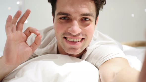 Okay Gesture by Handsome Young Man Lying in Bed