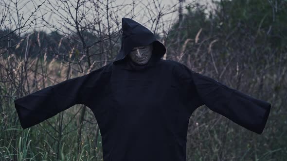 Horror figure in dark costume with hood. Portrait of scary ghost with outstratched arms