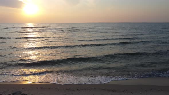 Sunrise on the sea beach. A light wind forms small waves that wash the sandy shore