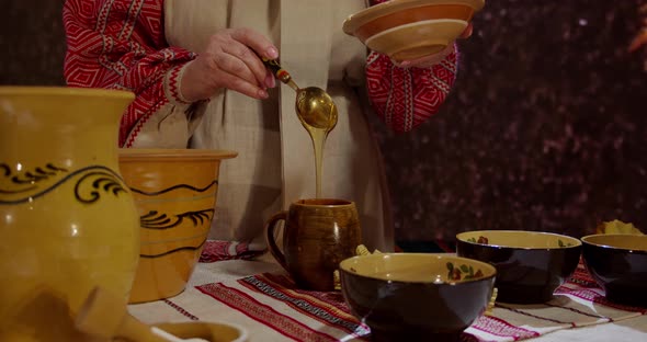 Woman In Traditional Ukrainian Embroidered Shirt Pour Honey Into Wooden Utensils