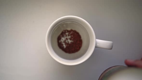 Man's Hand Pours Spoonful of Coffee and Cream Into Ceramic Mug