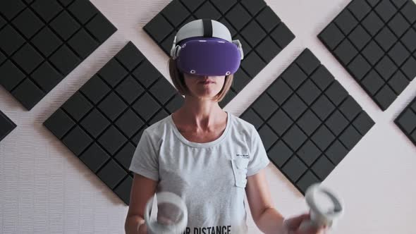 Young Woman in a VR Helmet Plays a Game at Home