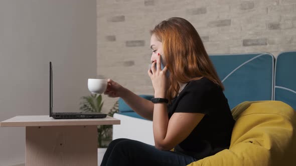 Young Woman Is Working at the Laptop While Is Talking on the Phone.