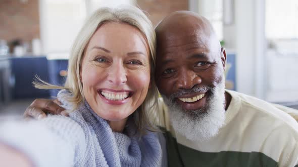 Happy senior diverse couple in living room sitting on sofa, making video call