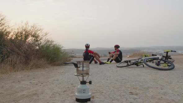 dolly shot of two professional young men bikers drinking coffe in the middle of the desert at sunris