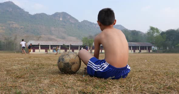 Rural Boy Sitting And Looking His Friend Playing Soccer