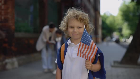 A Little Boy Standing Outside Near School with American Flag