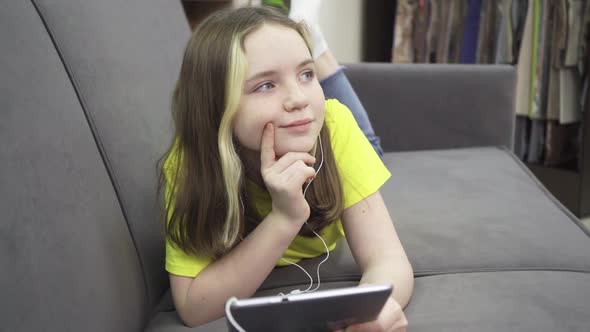 A Little Girl with Headphones Lying on the Couch