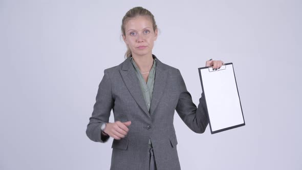 Young Serious Blonde Businesswoman Showing Clipboard and Giving Thumbs Down