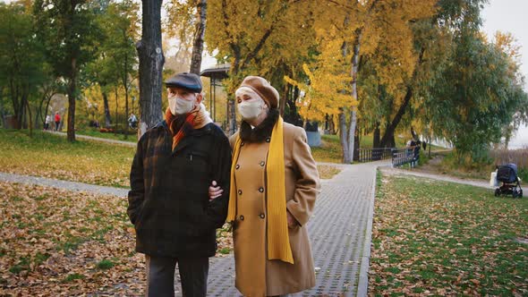 Elderly Spouses Grandparents in Protective Masks are Talking During a Walk in Autumn City Park