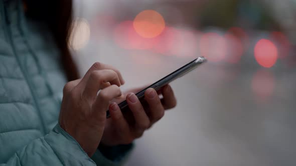 Closeup of a Woman's Hands with a Phone Against the Background of Blurred City Lights
