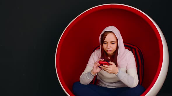 Woman Browsing Smartphone in Egg Armchair