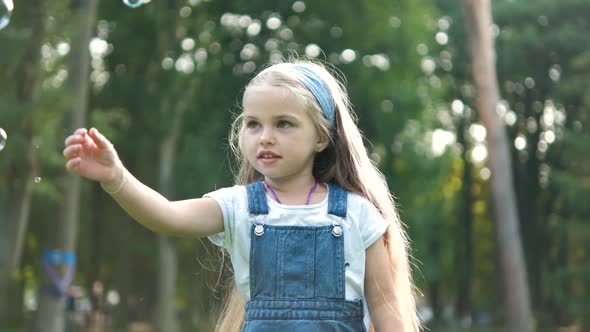 Little Happy Child Girl Chasing Soap Bubbles Outdoors in Summer Park