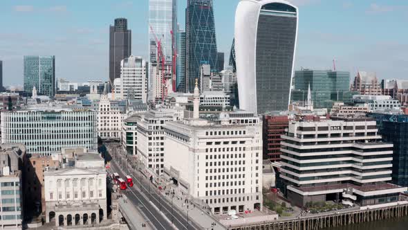 Rising drone shot from red buses on London bridge revealing city skyscrapers