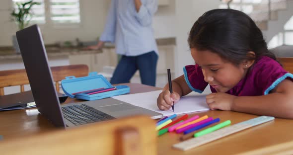 Hispanic girl sitting at table drawing with mother in background