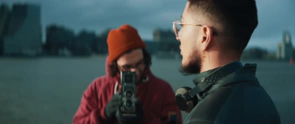 Young man moves around a male model and taking pictures with vintage camera