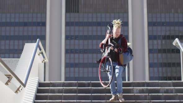 Thoughtful albino african american man with dreadlocks going down stairs with bike