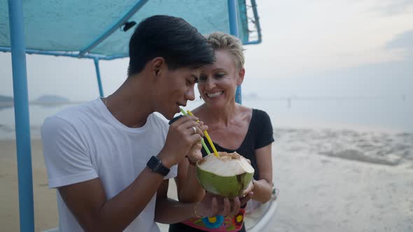 Married Interracial Couple with an Age Contrast Exchange Straws While Drinking Coconut Water on the