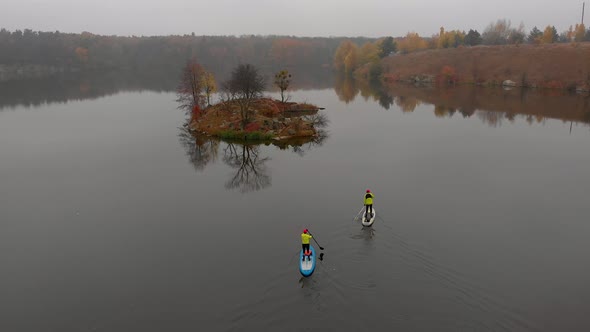 Man and Woman on Sup Paddle Boards at Wide River with Small Island on Golden Autumn Forest