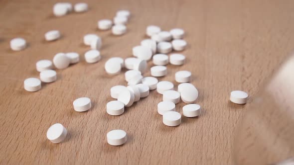 Medical pills are thrown in slow motion from a glass container on a wooden table