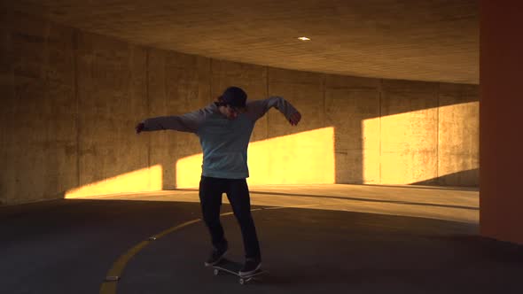 Silhouette of a young man skateboarding in a parking garage at sunset.