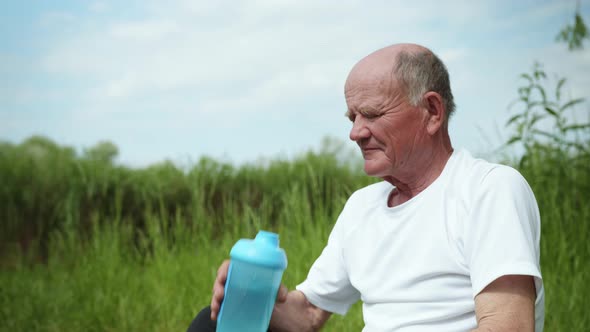 Healthy Elderly Man Restores Balance and Drinks Clean Water From a Bottle for Sports Nutrition After