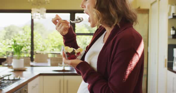 Profile of caucasian pregnant woman standing in kitchen and eating ice cream