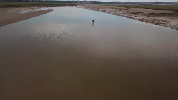 Man kayaking on meandering river, drone pans up to reveal kayaker and beautiful landscape in the bac