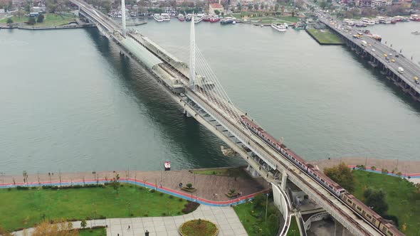 Aerial drone circling the Halic Metro Bridge as a train crosses the Bosphorus River during a cloudy