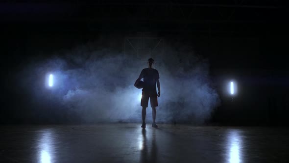 The Silhouette of a Basketball Player on a Dark Background with Smoke on the Basketball Court Throws