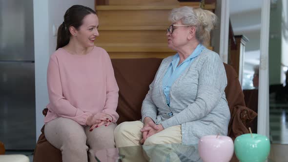 Portrait of Cheerful Laughing Caucasian Grandmother and Granddaughter Talking Sitting in Living Room