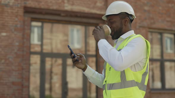 Happy Builder with Smartphone and Cup of Coffee Outdoors