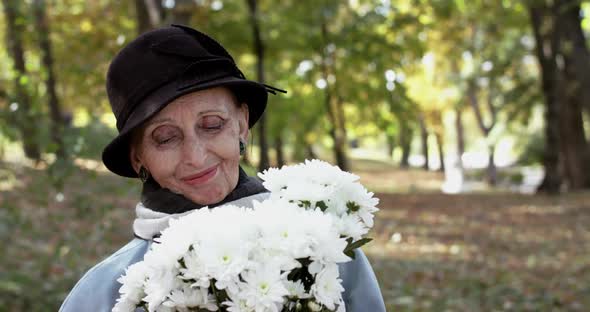 Elegant Lady in Hat with Bouquet of Flowers Smiling Looking at Camera in Park