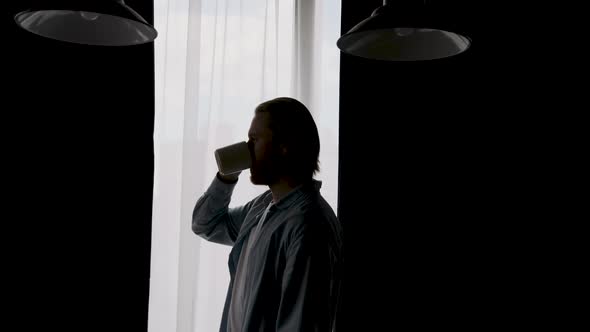 Silhouette of a Man Drinking Coffee Near the Window at Home
