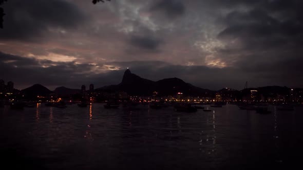 Sunset time lapse on Guanabara bay in Rio de Janeiro with city lights turning on and Christ statue o