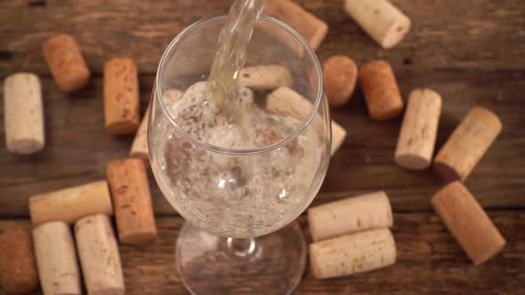 Wine is poured into a glass against the background of old wooden boards and wine corks. Slow motion.