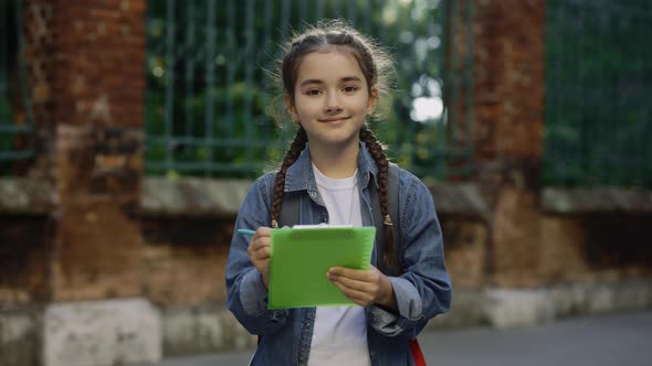 Portrait of Lillte Cute Casual Girl Braids with Schoolbag Standing Schoolyard Smilling and Writting