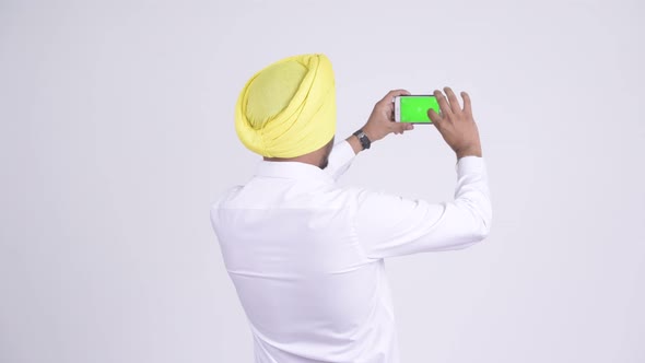 Rear View of Indian Sikh Businessman Taking Picture with Phone