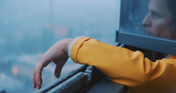 Young man wearing yellow raincoat stretches out his arm of the window