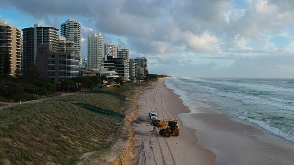 Heavy construction equipment picking up rubbish from a beach that was damaged by a recent cyclone
