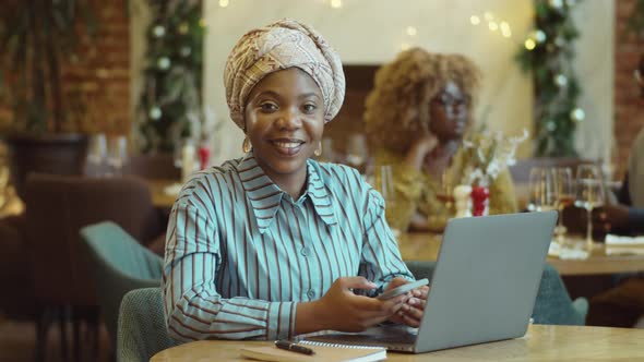 Portrait of Smiling Black Woman with Laptop and Phone in Cafe