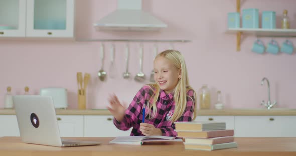 School Kid Greets Online Teacher While Studying Online on Laptop at Home. Blonde 10 Years Old Girl