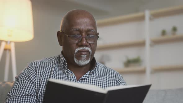 Close Up of Concentrated Senior African American Man Wearing Eyeglasses Reading Interesting Book at