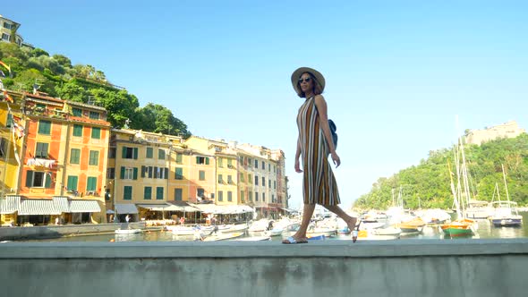 A woman walking wearing hat and backpack purse traveling, Portofino, Italy, luxury resort, Europe