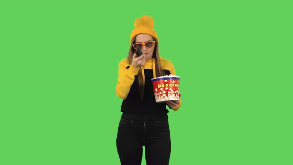 Modern Girl in Yellow Hat in 3D Glasses Is Watching TV and Eating Popcorn with TV Remote in Her Hand