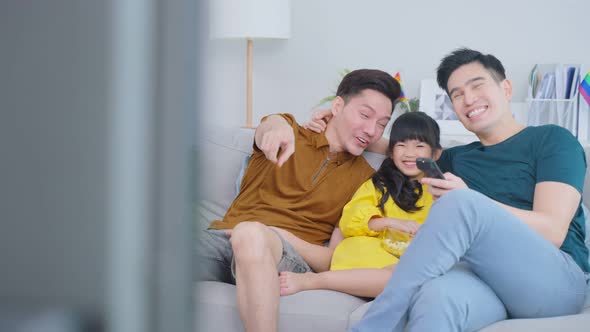 Asian male gay family with young daughter enjoyment watch movie in vacation at living room.