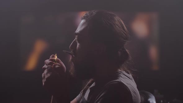 A Man with a Beard Looks at the Monitor Turns Sideways Lights a Cigarette Lets Out a Lot of Smoke